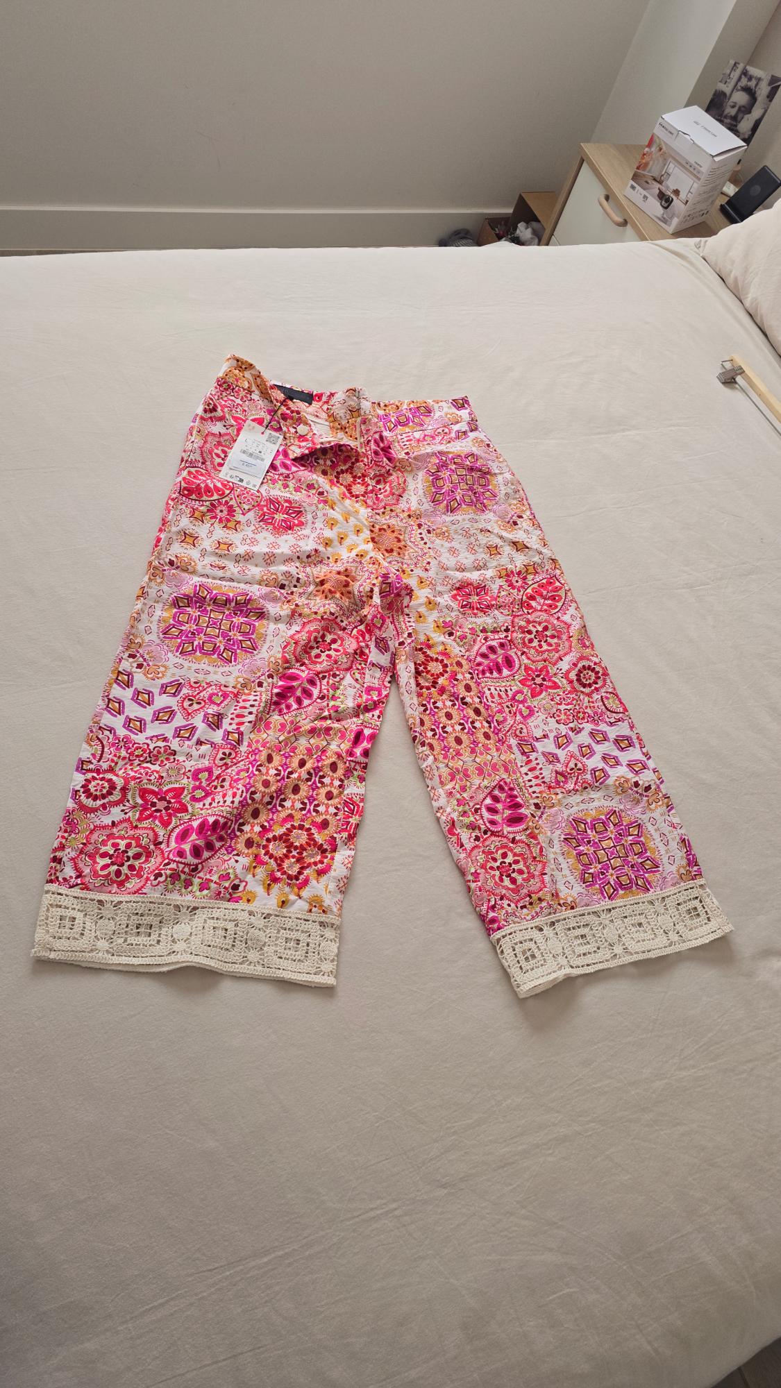 Floral print shorts in pink and orange tones, with lace detail on the hem, on a beige bed.