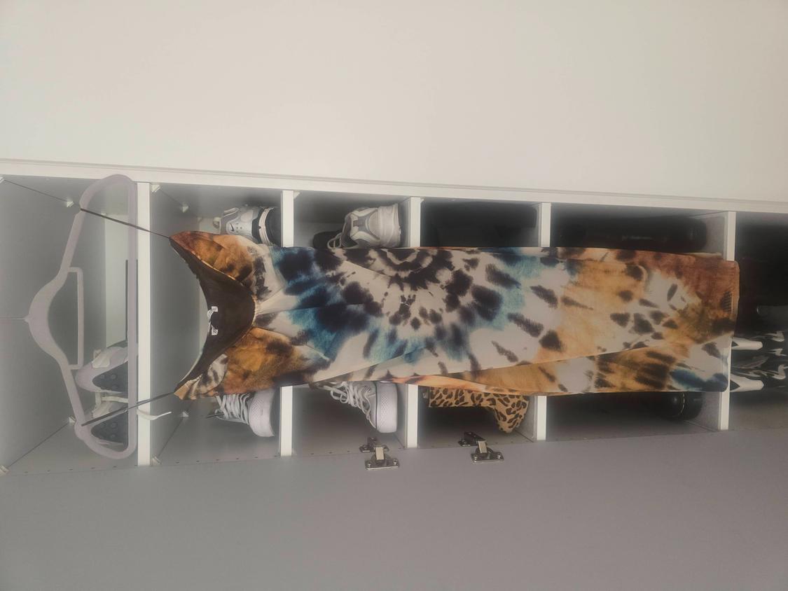 Φόρεμα με τιράντες και στάμπα tie-dye σε αποχρώσεις του καφέ, του μπλε και του μαύρου, κρεμασμένο σε μια λευκή ντουλάπα με ράφια.