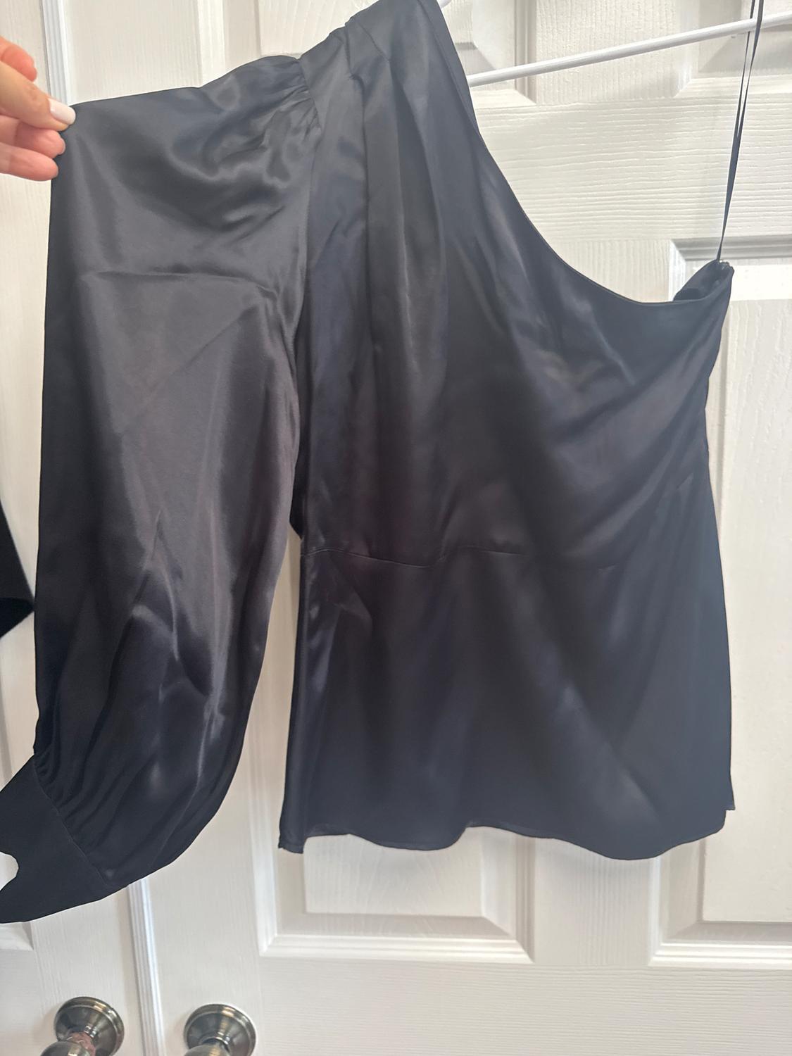 Black satin one-shoulder long-sleeved blouse, hanging on a hanger in front of a white door.