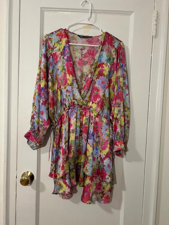 Colorful floral short dress with a V-neckline and long sleeves, hanging on a white hanger over a white door.