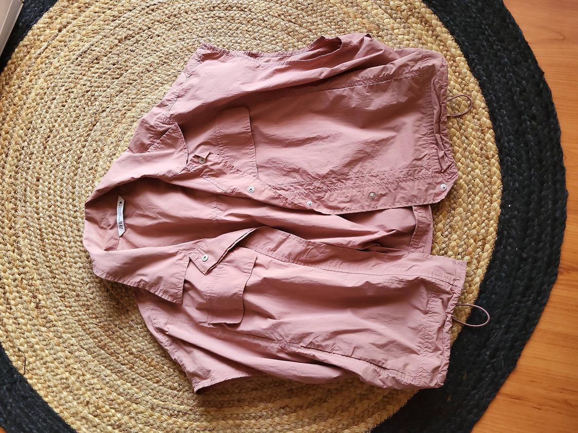 Pink crumpled shirt on a round jute rug with a black border. Visible label on the inside of the collar.