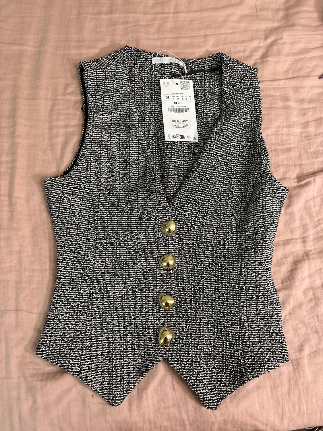 Textured waistcoat in black and white with gold buttons on pink fabric. Text: ZARA S US $45.90 UK £25.99.