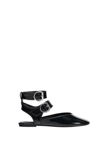 Black flat shoe with double straps and silver buckles on a white background. Elegant and modern design.