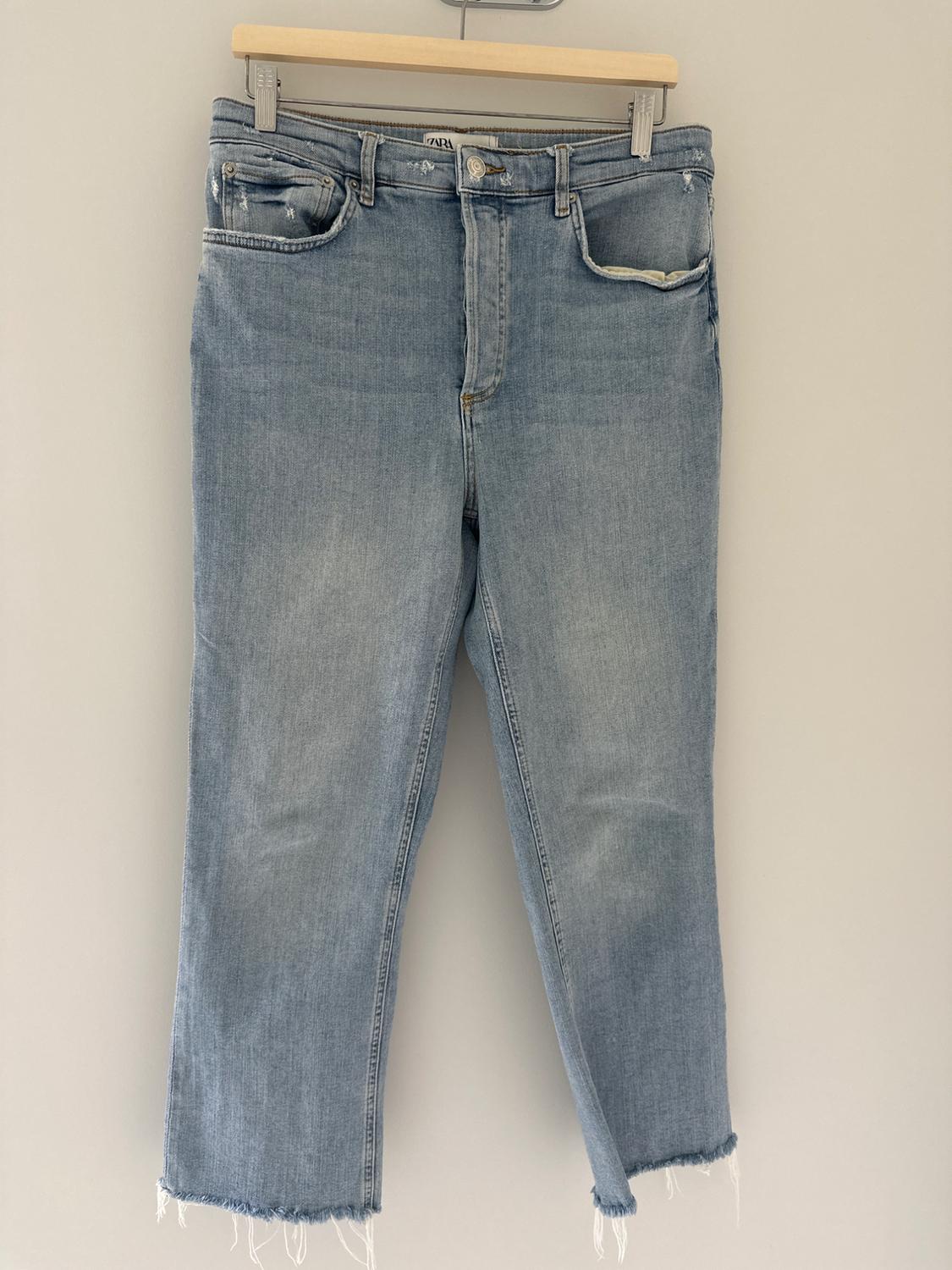 Light blue jeans with frayed hem hanging on a wooden hanger on a white background.