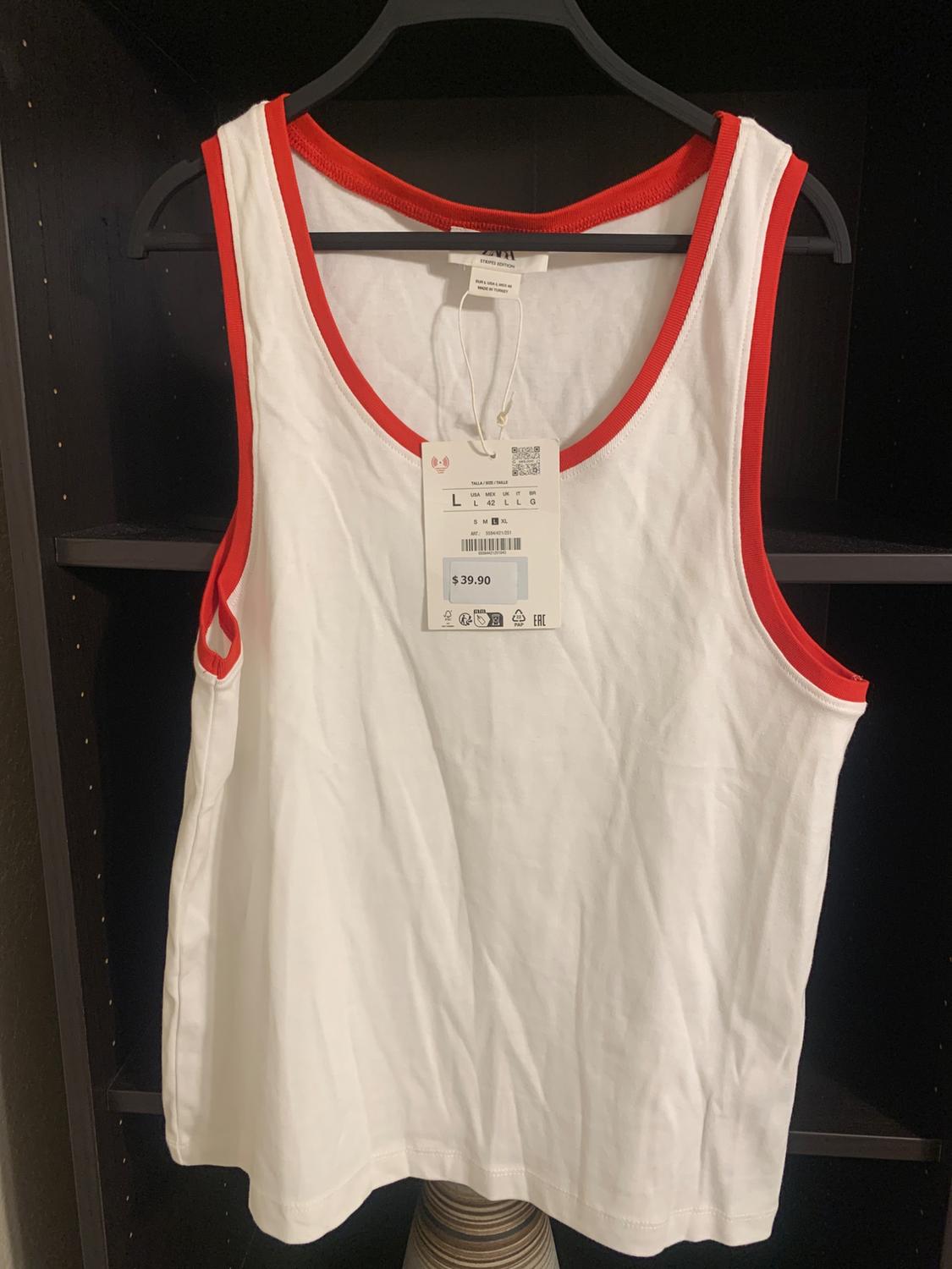 White sleeveless top with red trim, hanging on a black hanger. Visible tag with a price of $39.90. Dark background.