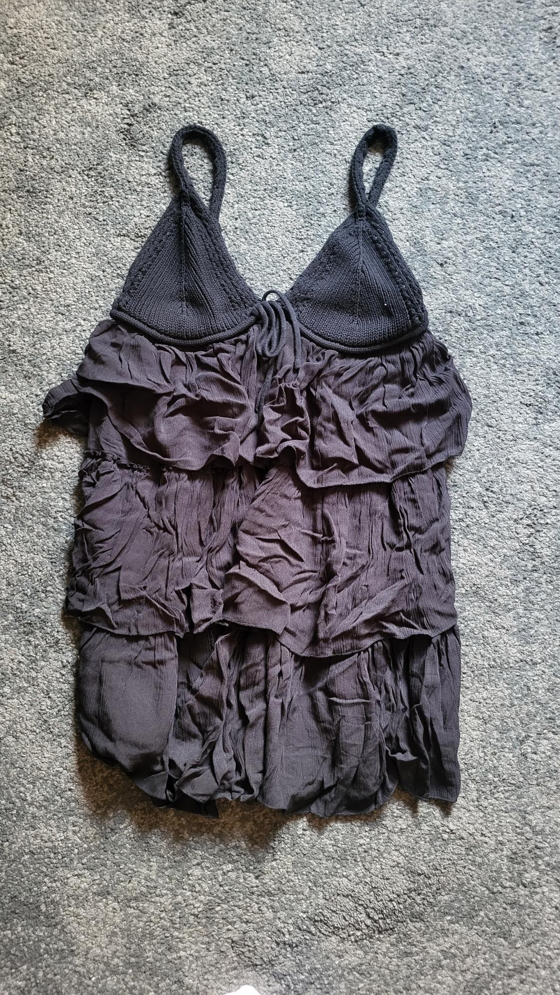 Black dress with spaghetti straps and frills, on a grey carpet background.