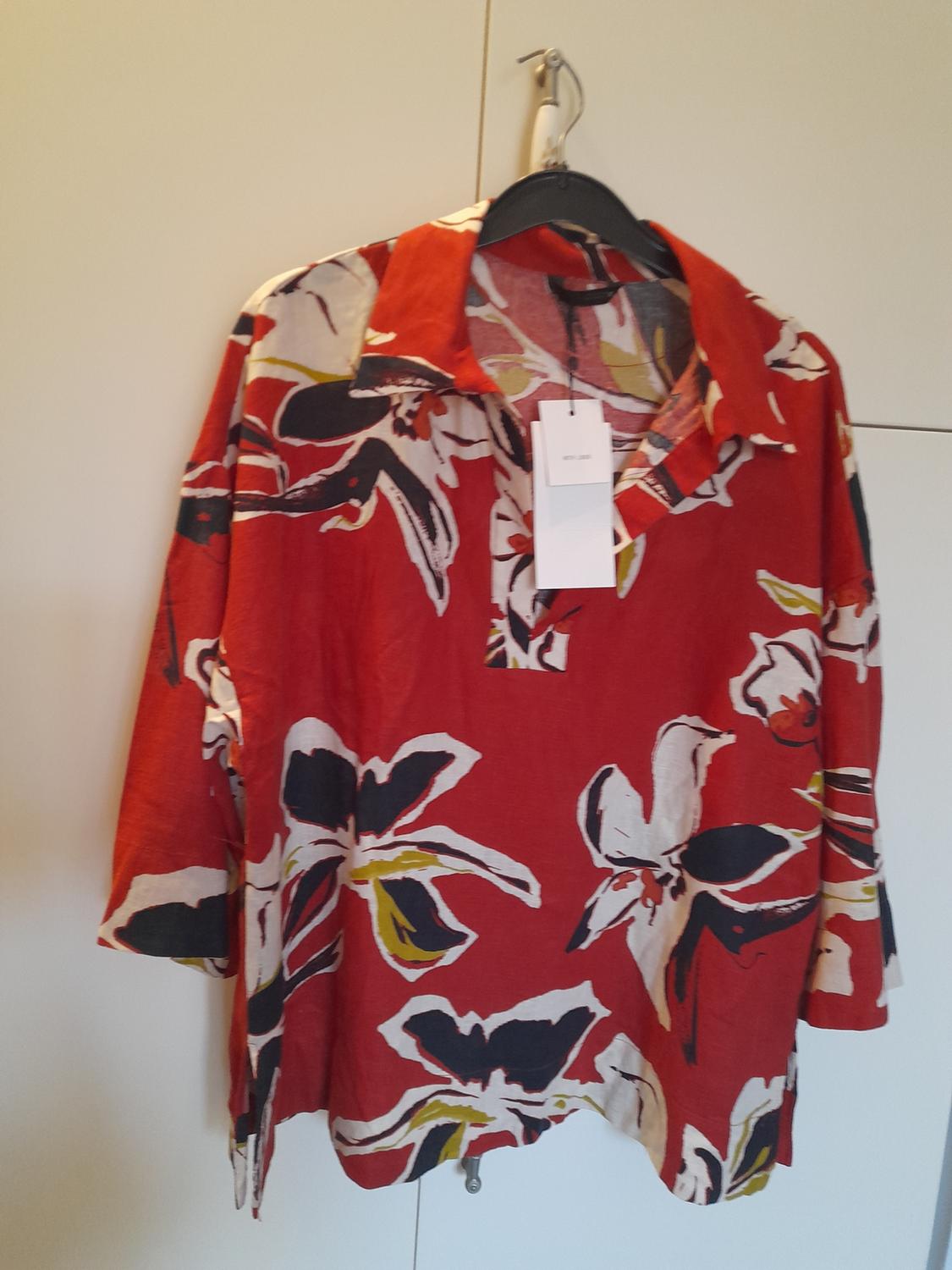 Red three-quarter sleeve shirt with a black and white floral print, hanging on a black hanger against a white wardrobe background.