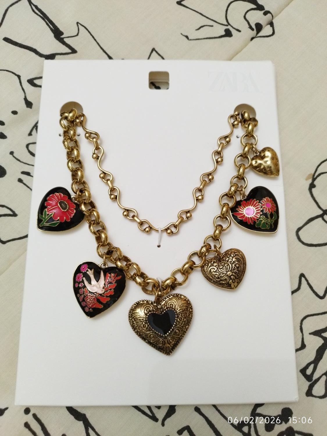 Gold necklace with heart pendants decorated with flowers and birds on a black background. Date on image: 06/02/2026 15:06.