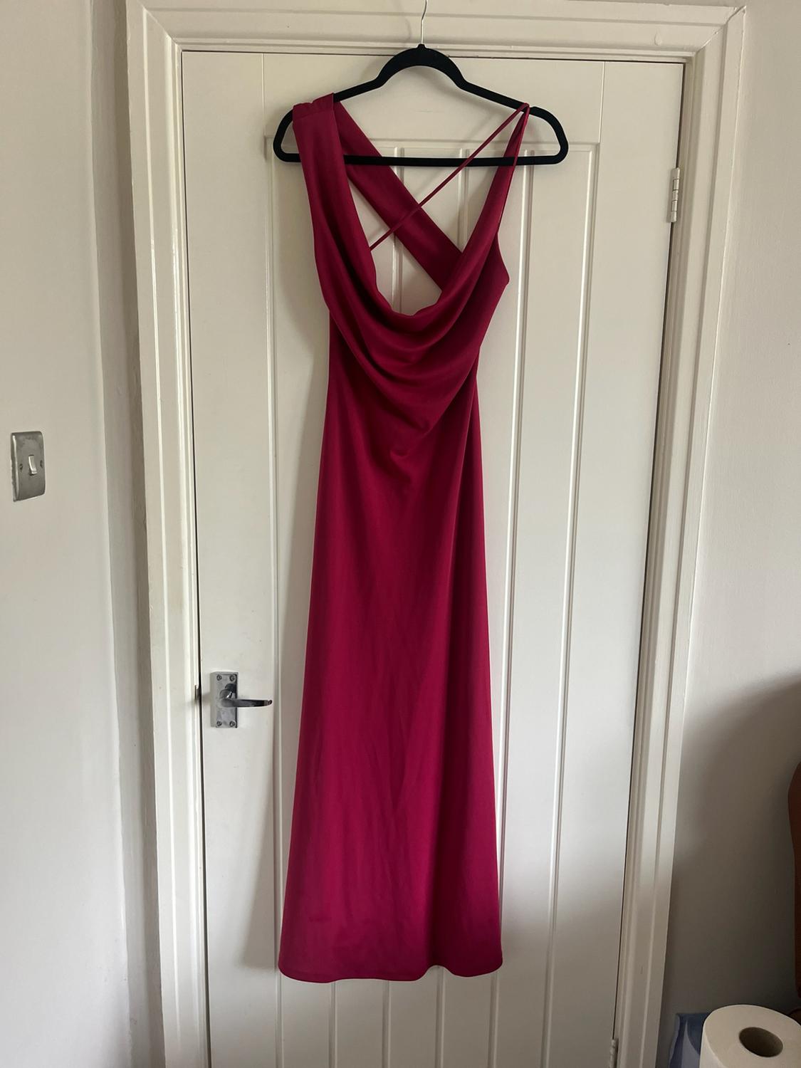 Magenta maxi dress with a draped neckline and fine crossed straps, hanging on a black hanger over a white door.