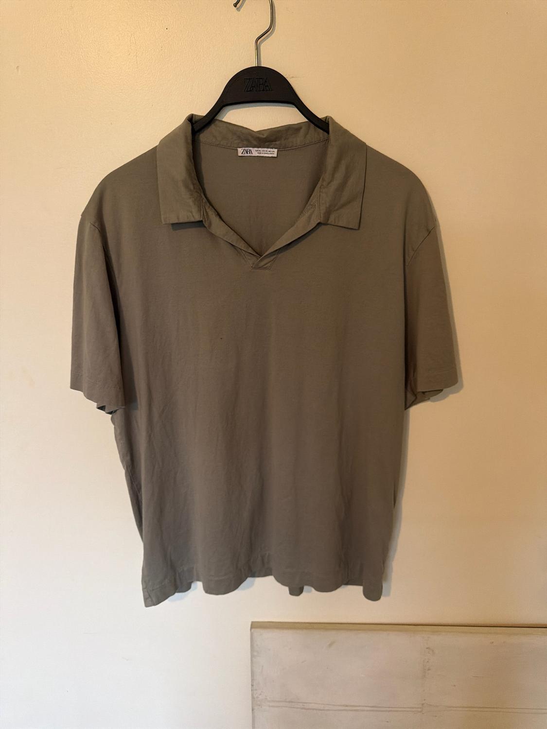 Olive green short-sleeved casual polo shirt hanging on a black hanger against a beige wall. Text: ZARA.