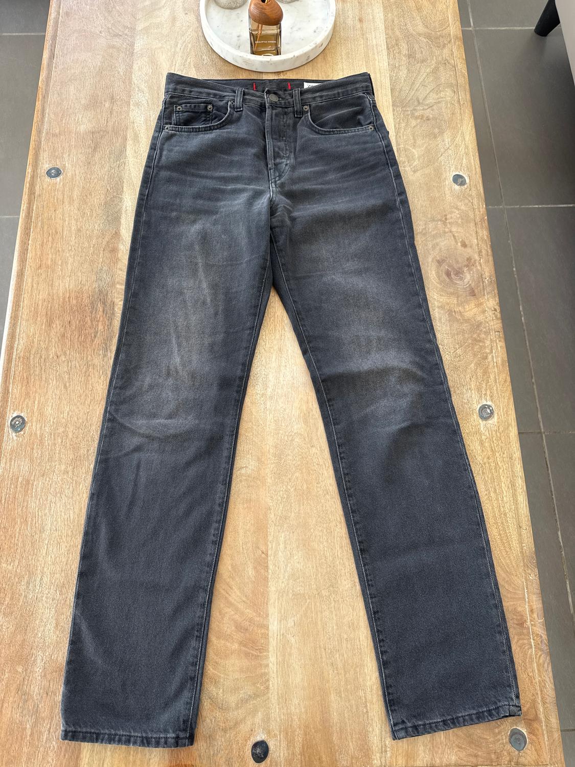 Distressed black denim jeans on a light wooden table. In the background, a tray with decorative items.