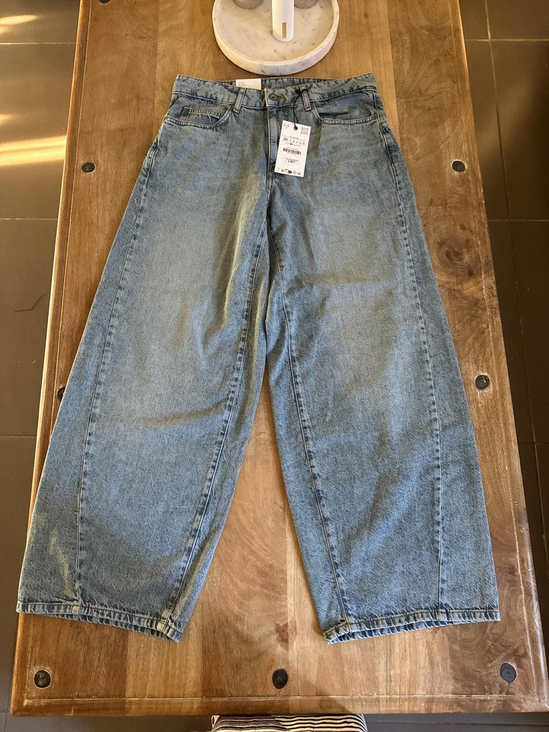 Light blue wide-leg jeans with front seams and labels, laid out on a wooden table.