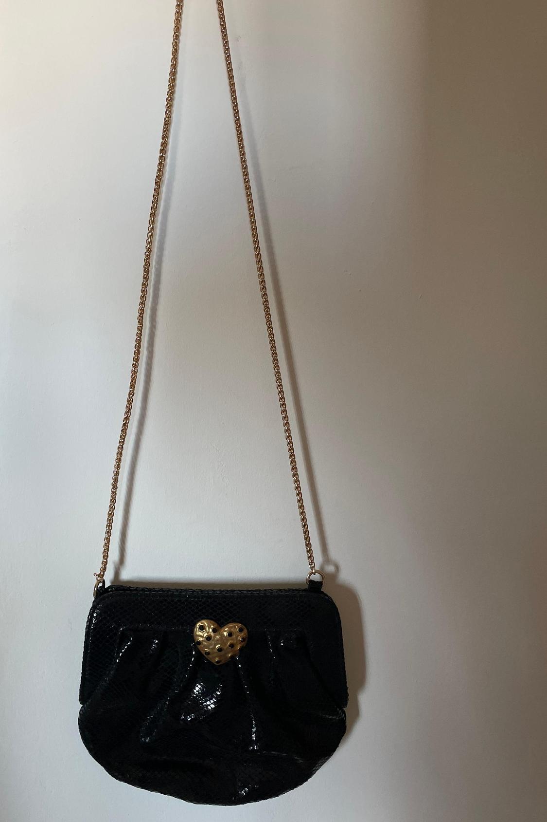 Front view of a black handbag with a gold chain and a gold heart-shaped clasp.