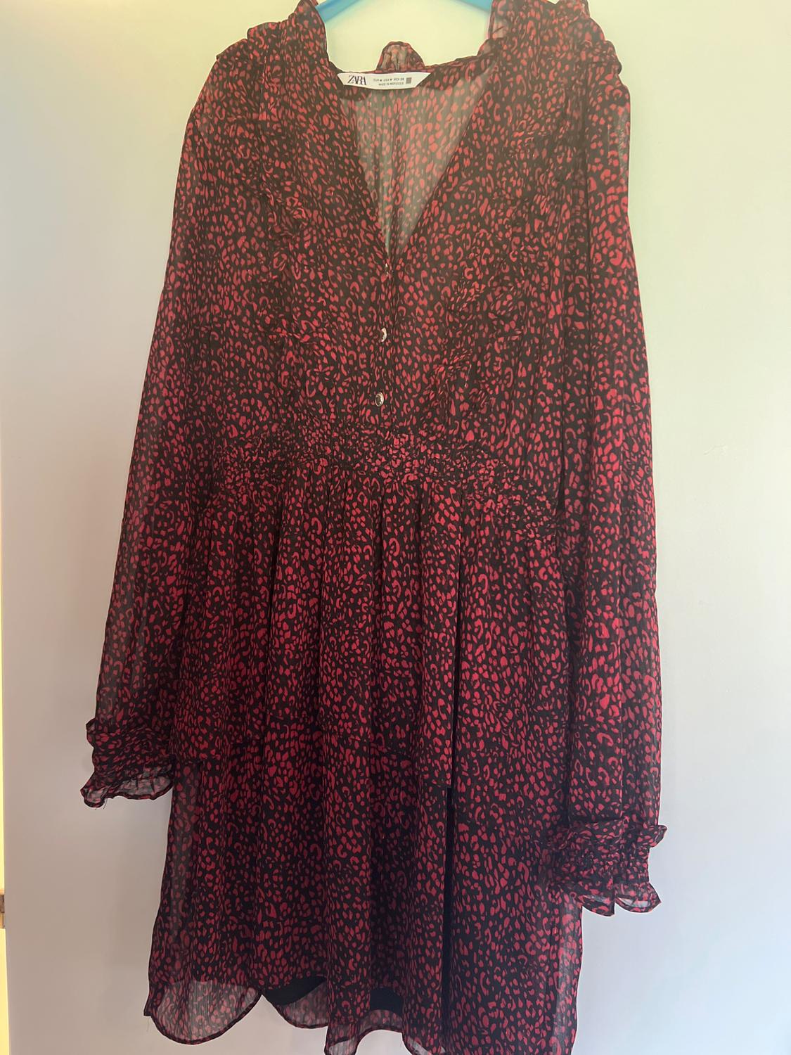 Red and black animal print long-sleeved dress with V-neck, buttons and frills, hanging on a hanger. Label with the text ZARA.