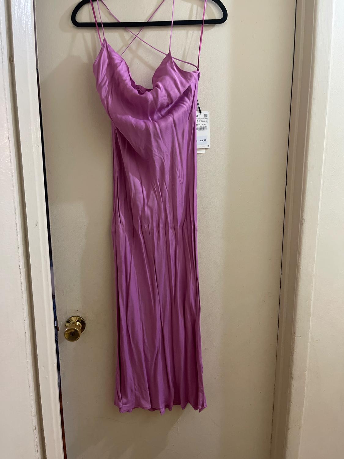 Lilac maxi dress with thin criss-cross straps, hanging on a black hanger over a white door. Visible tag with price.