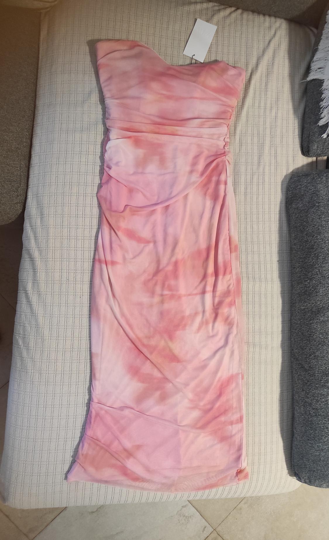 Strapless maxi dress in shades of pink and orange on a beige sofa. White label visible at the top.