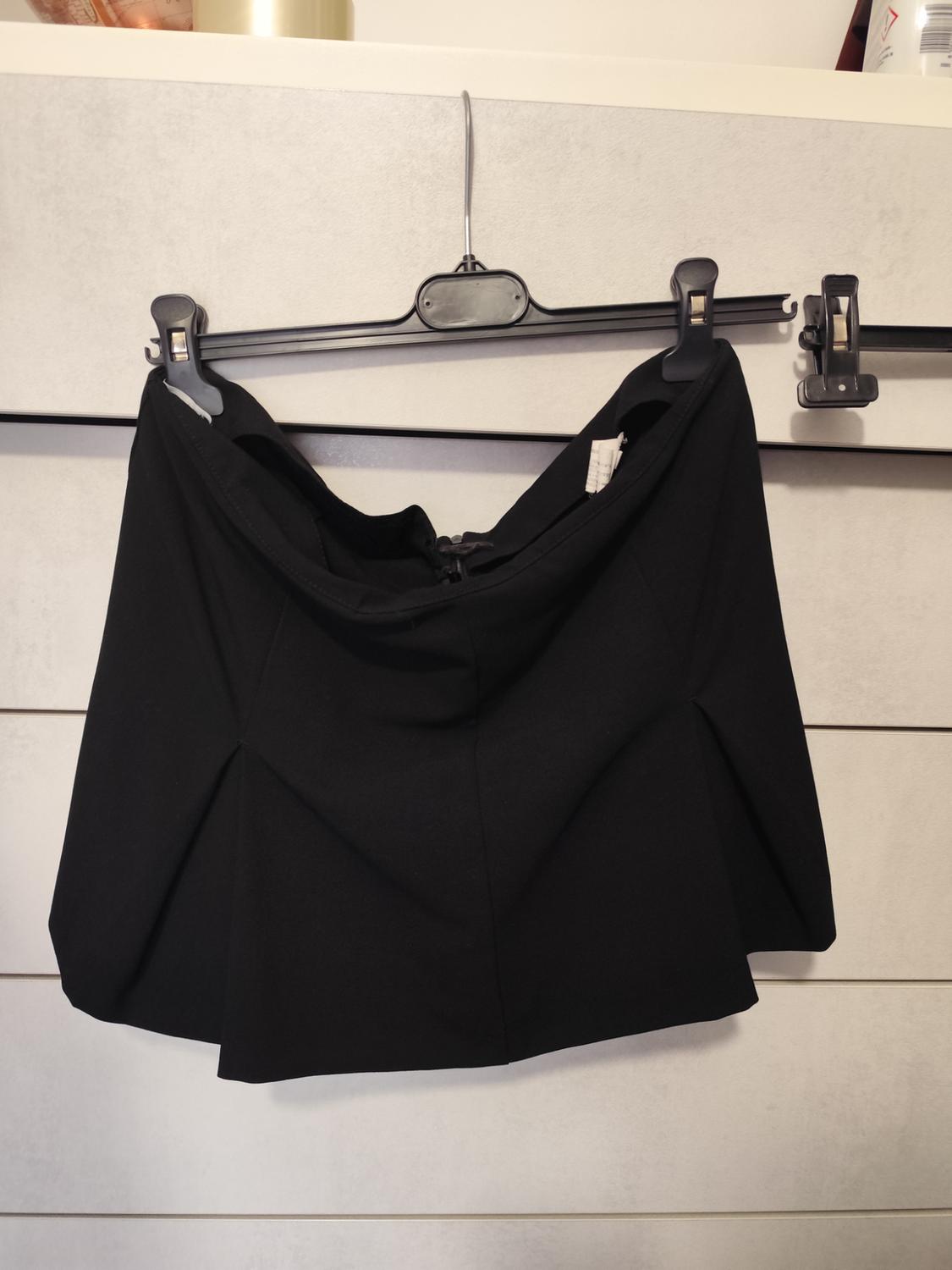 Black skirt hanging on a hanger against a background of grey drawers. Top of a jar visible in the top left corner.