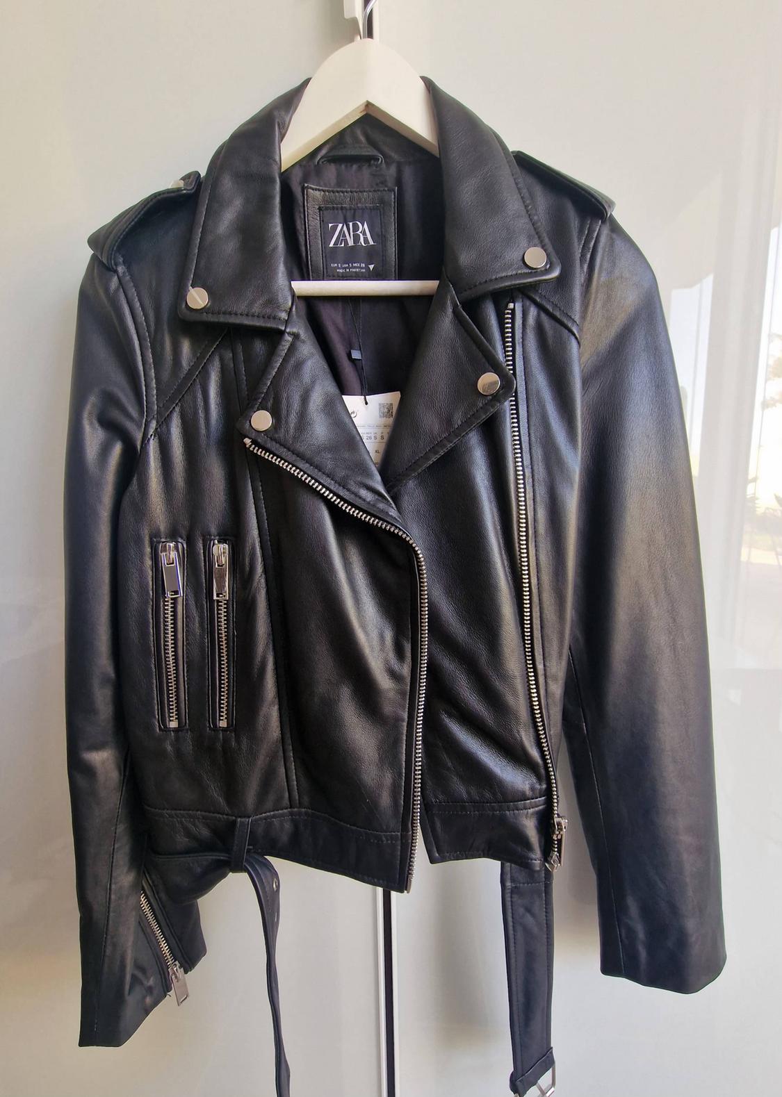 Black biker-style jacket on a white hanger. Silver zip and belt details. ZARA label inside.