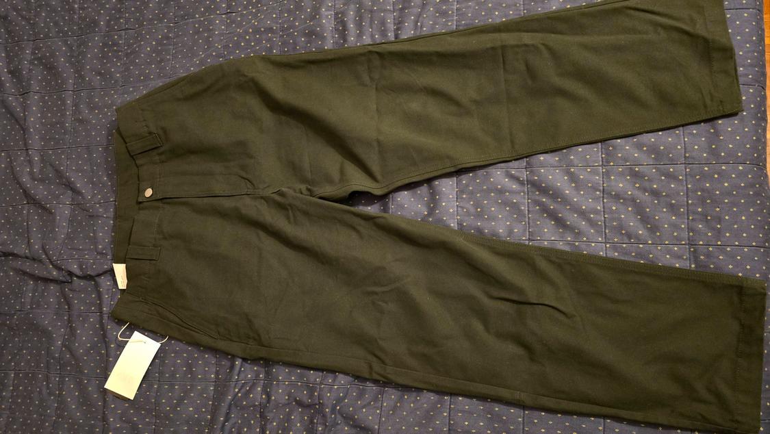 Green straight-cut trousers on a blue bedspread with gold dots. White label hanging from the waistband.