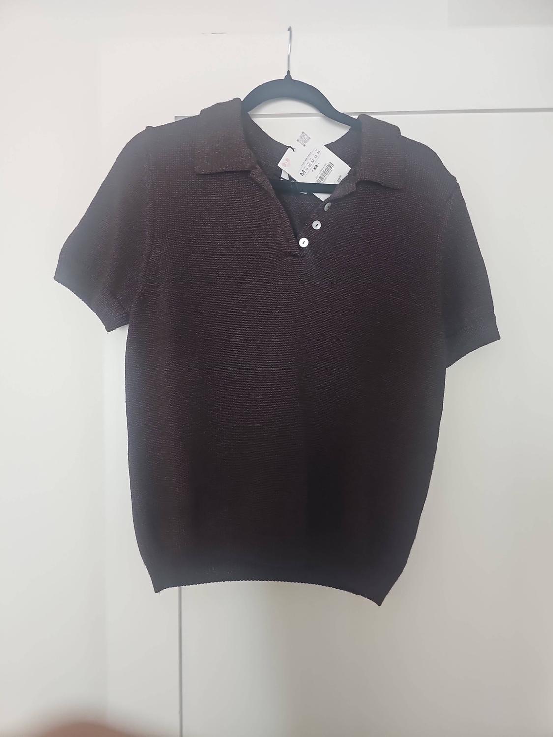 Dark brown short-sleeved knitted polo shirt with a collar and buttons, hanging on a black hanger over a white door.