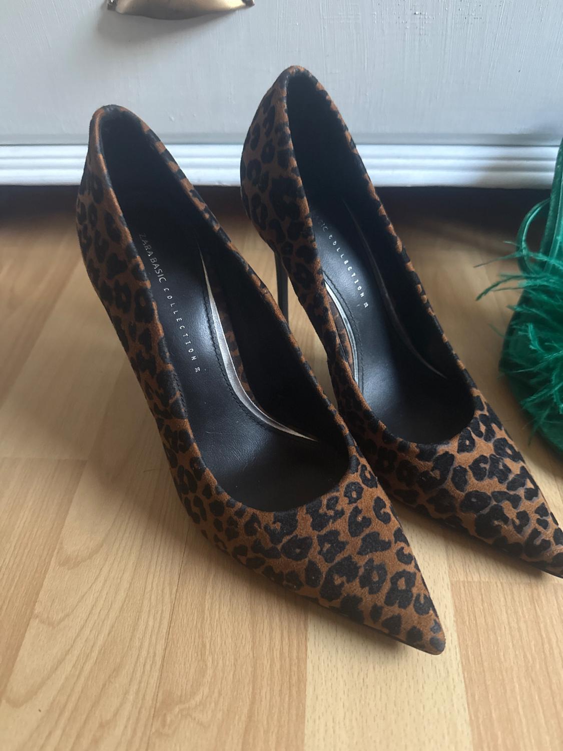 Leopard print high heels on a wooden floor. Visible text: "ZARA BASIC COLLECTION".
