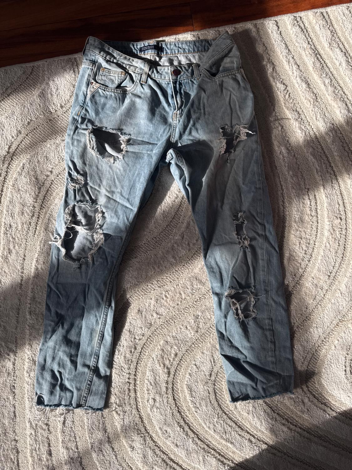 Front view of distressed denim jeans with rips on the legs and front pockets.
