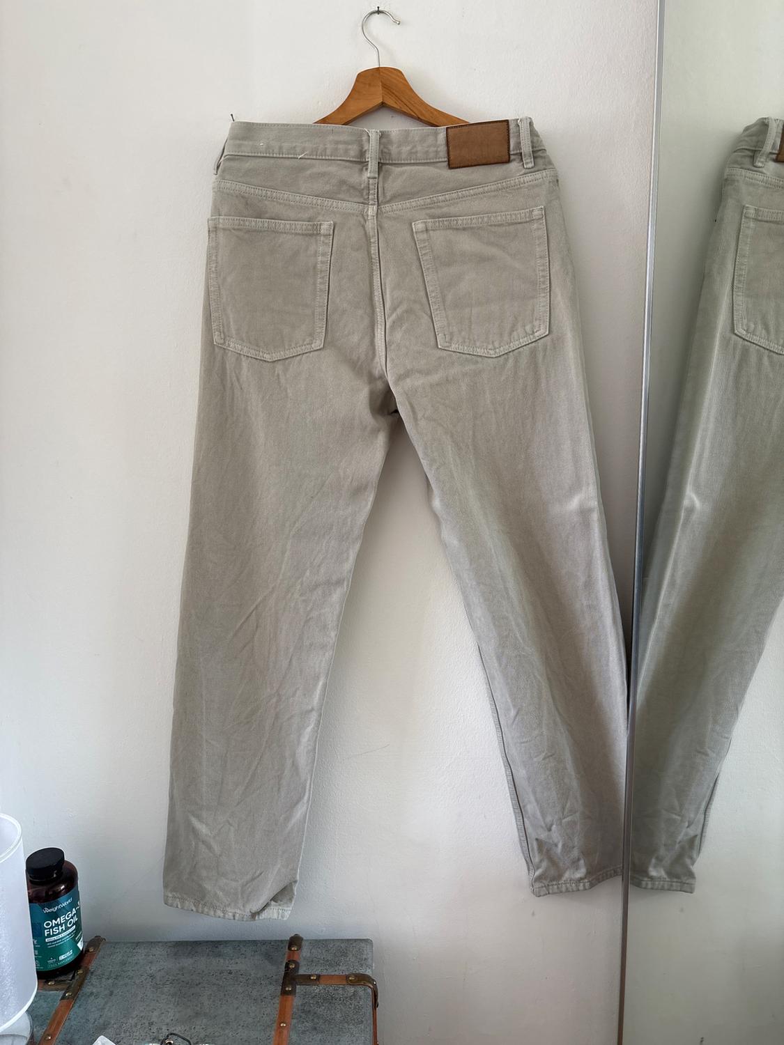 Grey trousers seen from behind on a wooden hanger against a white wall next to a mirror. Below is a trunk and a tub of OMEGA FISH OIL.