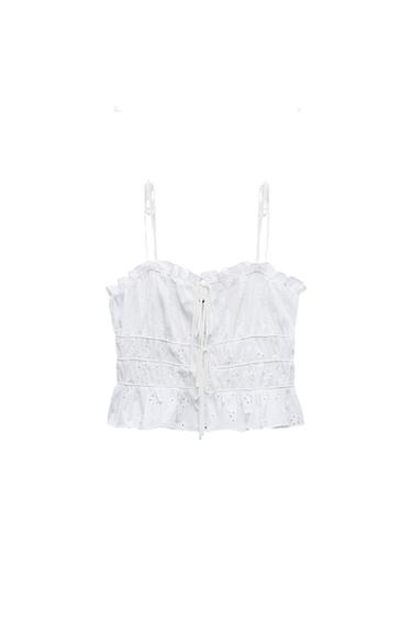 White top with tie straps, ruffled neckline and hem, front drawstring, gathered waist and Swiss embroidery fabric on a white background.