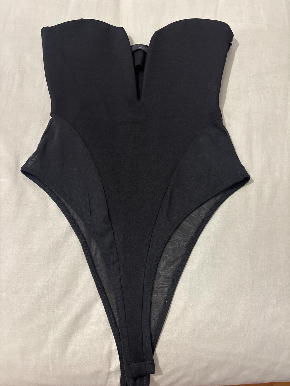 Black bodysuit with a deep V-neck sweetheart neckline and semi-sheer mesh side panels, spread out on a light sheet.
