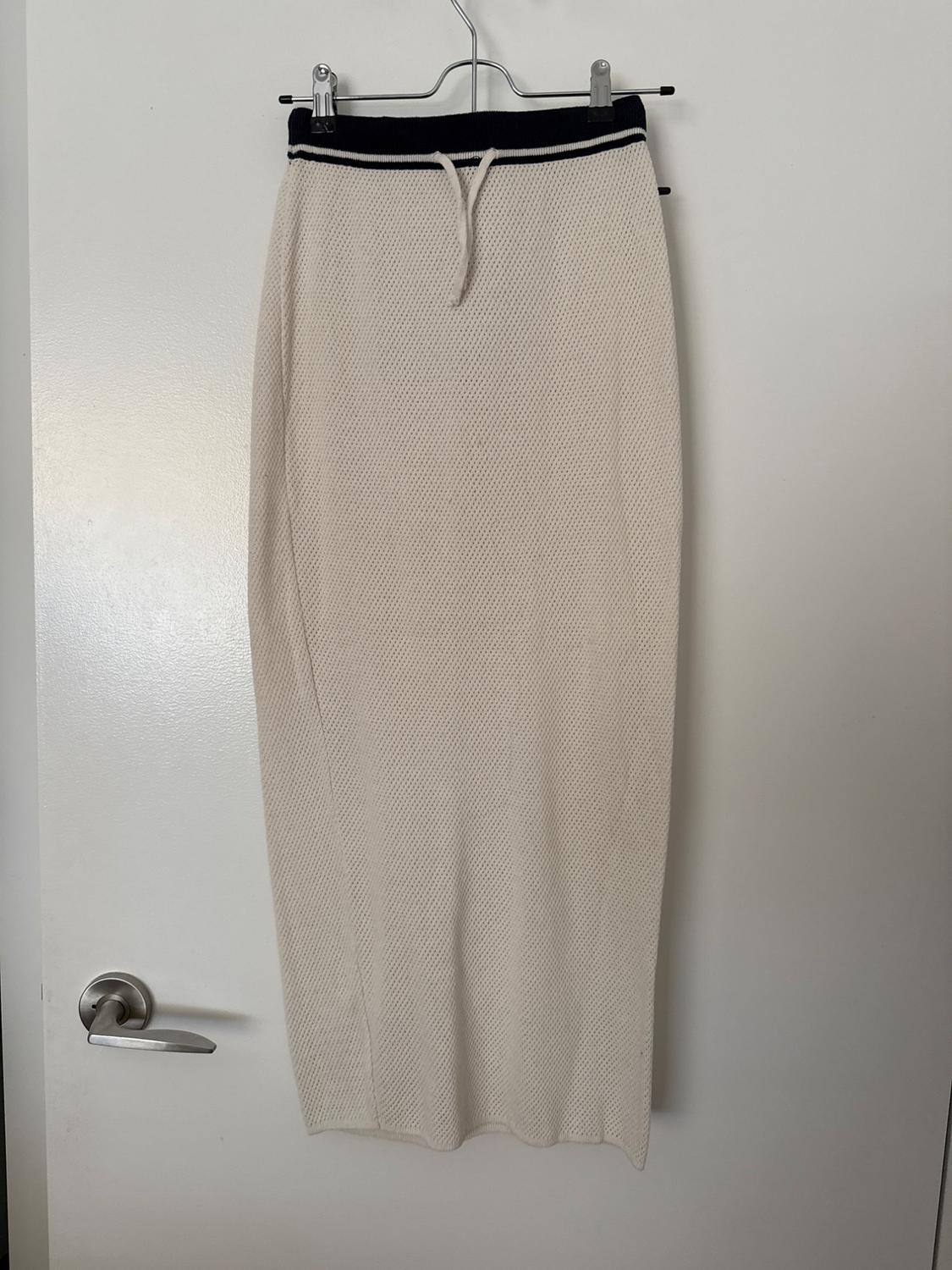 Cream knitted maxi skirt with a dark elasticated waist and drawstring, hanging on a white door with a silver handle.