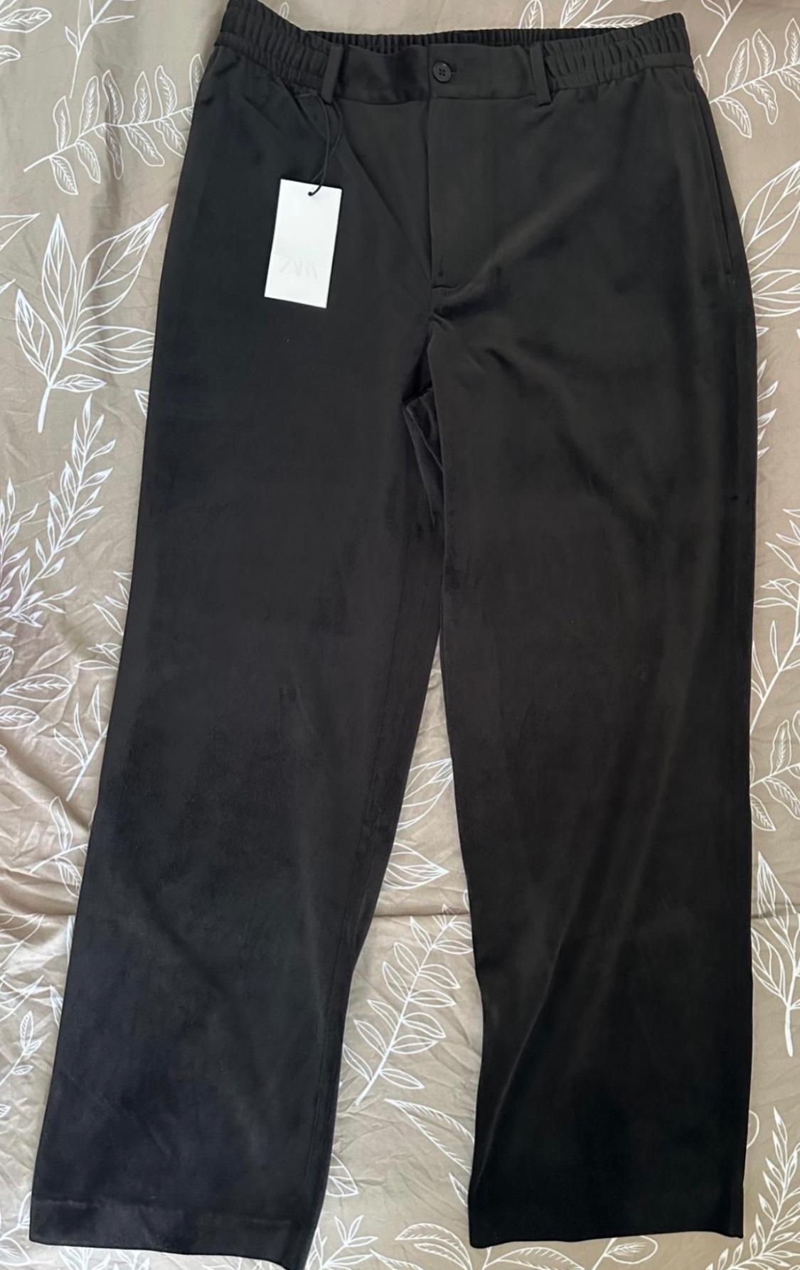 Black trousers with an elasticated waistband and ZARA label, against a beige background with a white leaf print.