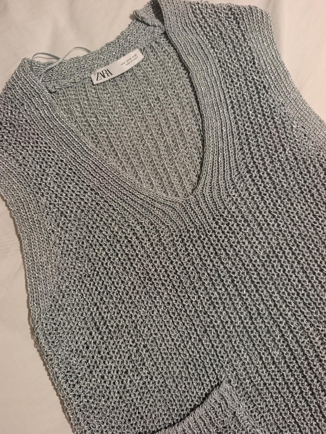 Grey knitted V-neck waistcoat, visible label with "ZARA" and "MADE IN CHINA" text, on a light background.