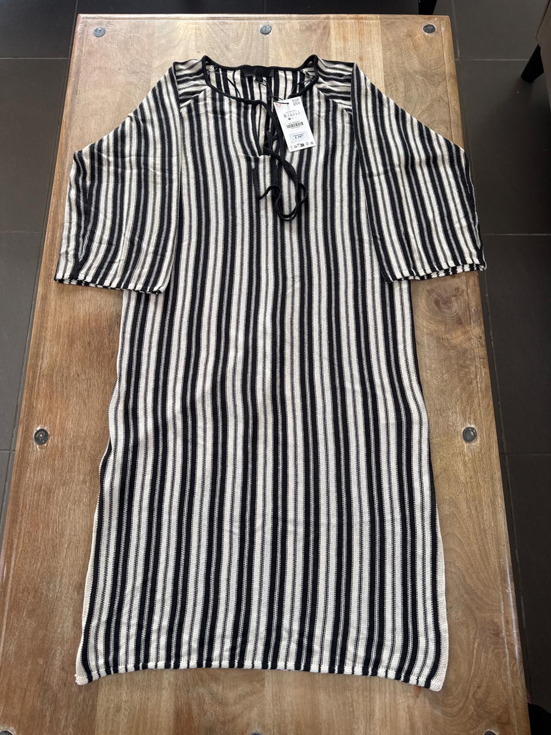 Black and white vertical striped dress on a wooden table. Visible tag on the collar with price details.