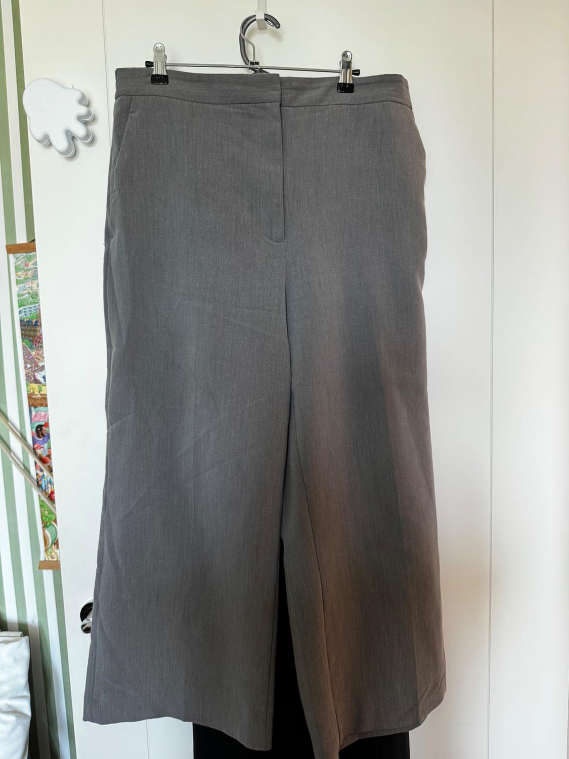 Grey trousers hanging on a hanger against a white background with green stripe details and a white hand-shaped ornament.