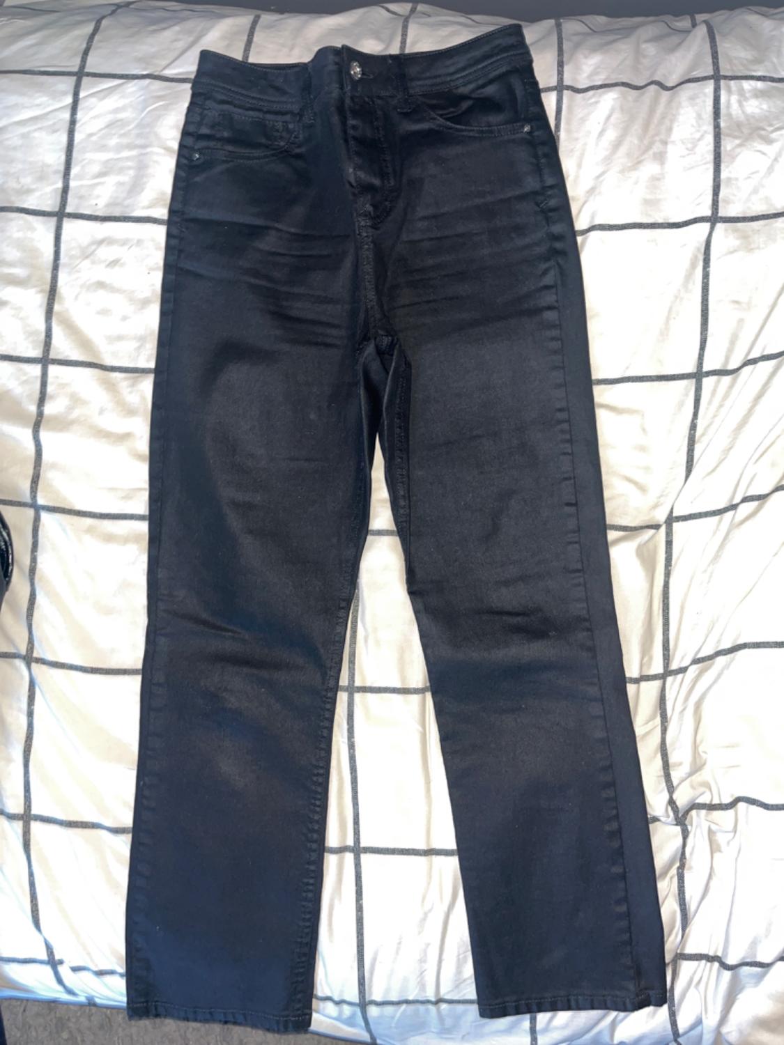 Front view of black pants with front pockets and button closure.