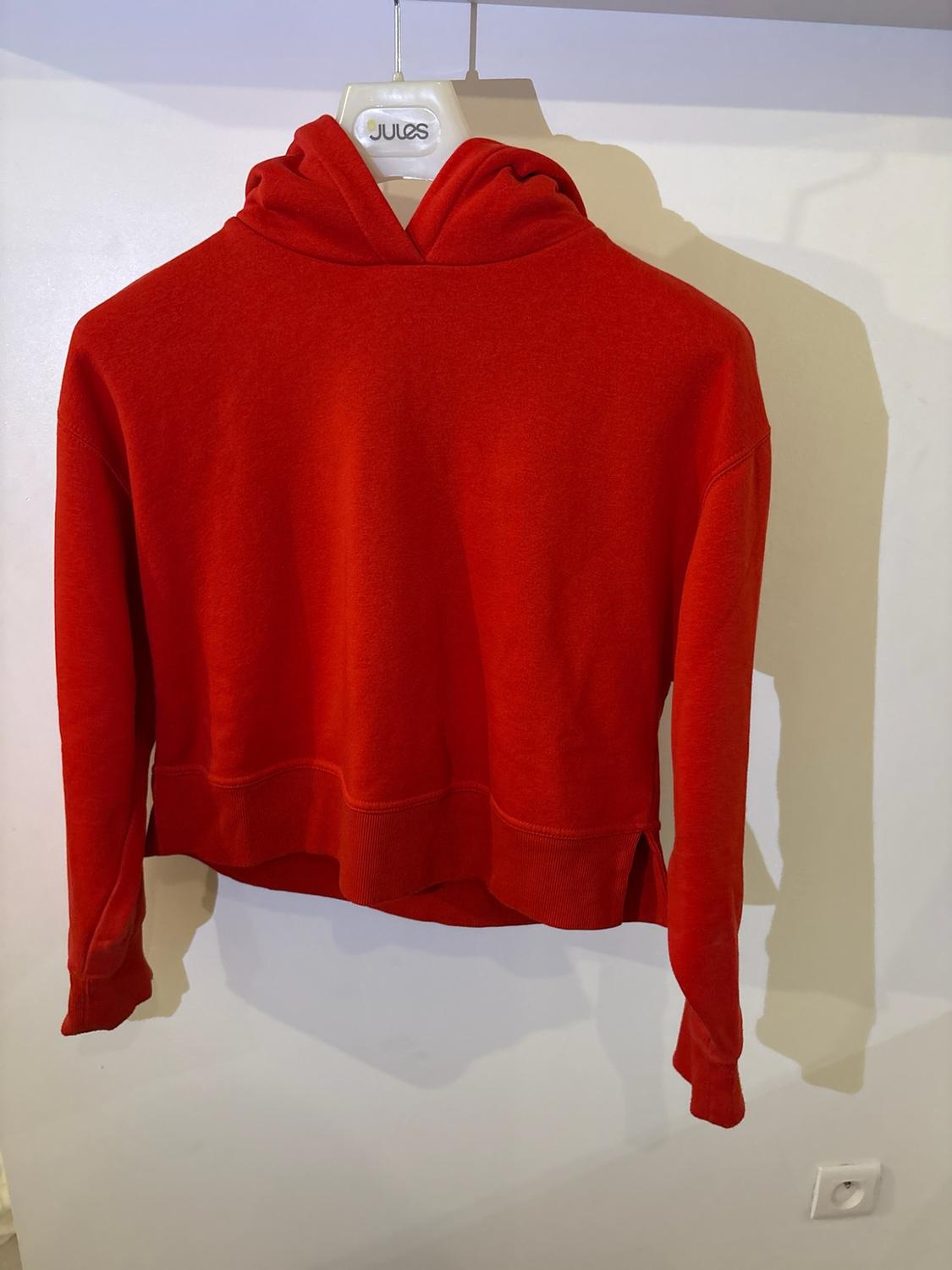 Red cropped hoodie hanging on a hanger with the text Jules against a white wall.