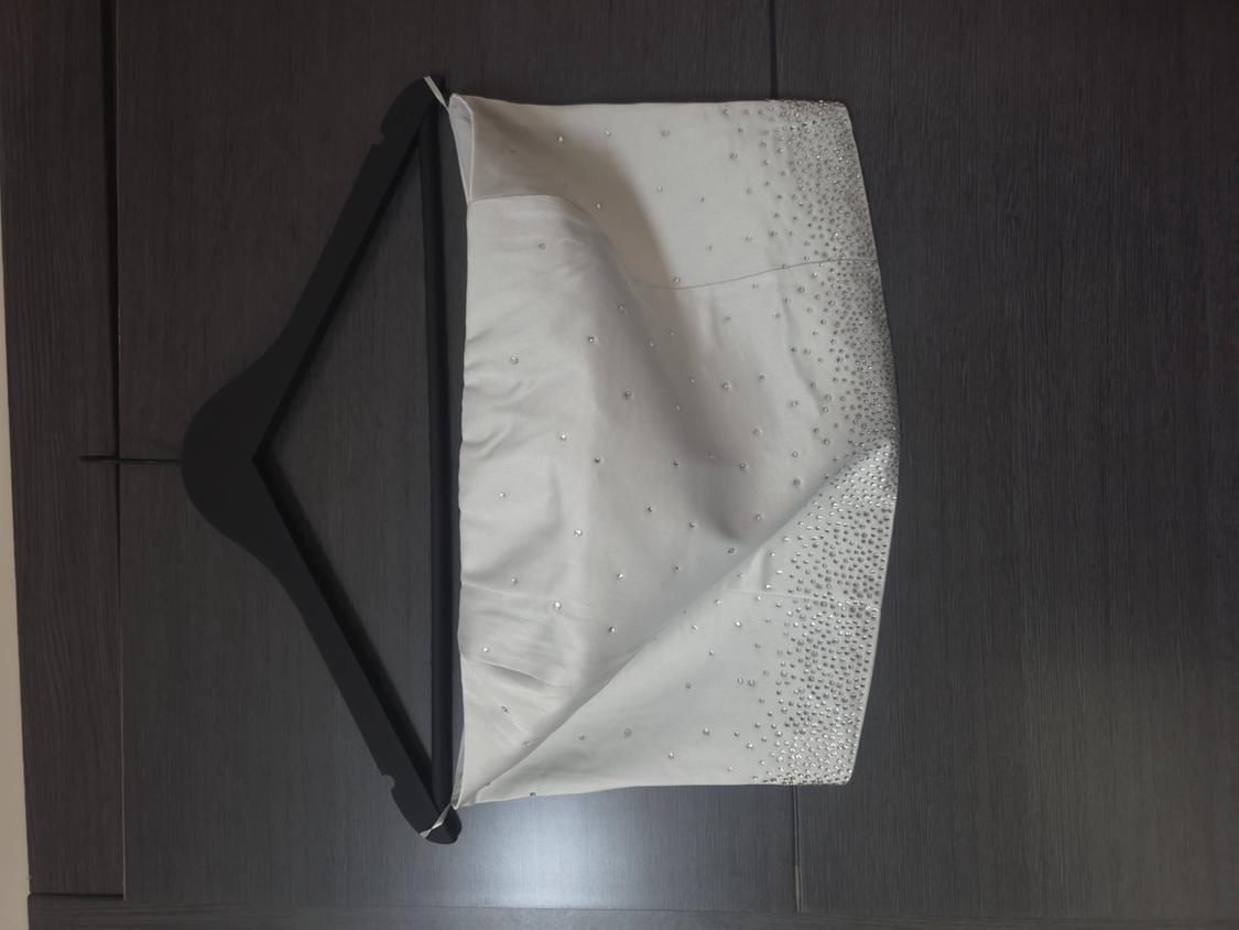 White garment with sparkling beading concentrated at the hem, hanging on a black hanger against a dark wooden surface.