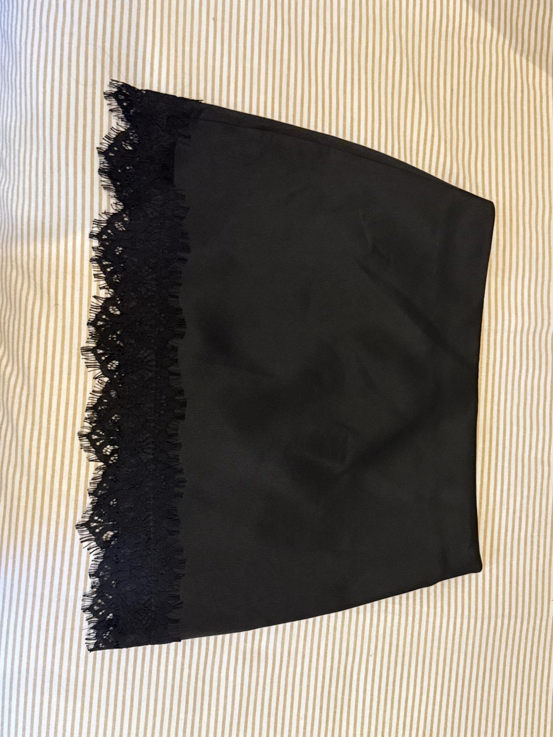 Black skirt with a lace hem, laid out on a light-striped surface. Relaxed style.