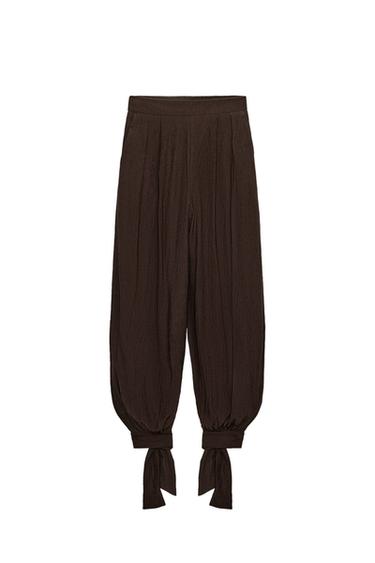 Front view of dark brown trousers with an elasticated waist, front pleats, front pockets, and tie cuffs.
