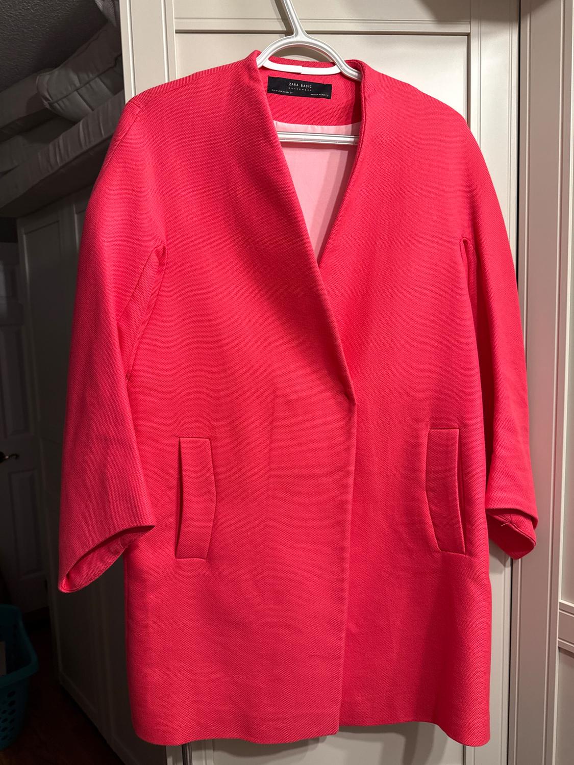 Red coat hanging on a white hanger, with front pockets and no buttons, against a white closet background.