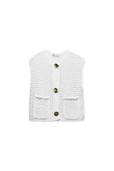 Front view of a white knitted waistcoat with gold buttons and front pockets.