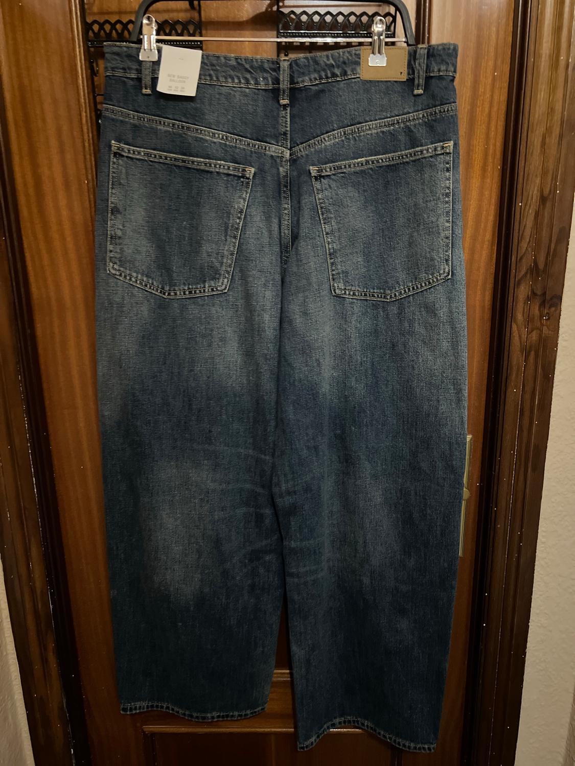 Rear view of a pair of blue jeans hanging on a wooden door. Shows pockets and a label bearing the text NEW BAGGY BALLOON.