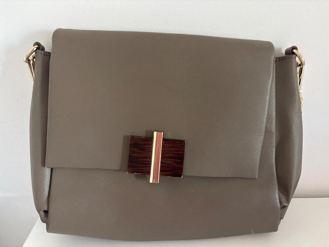 Brown shoulder bag with a gold metal clasp and a wooden detail on the front, on a white background.