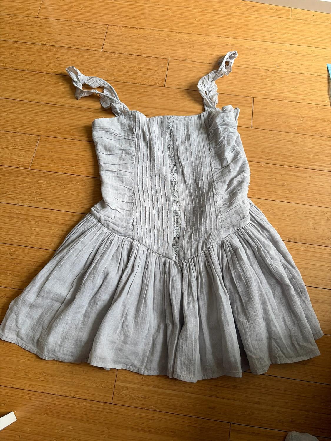 Light gray short dress with ruffled straps, ruched bodice, and flared skirt, on a wooden floor.