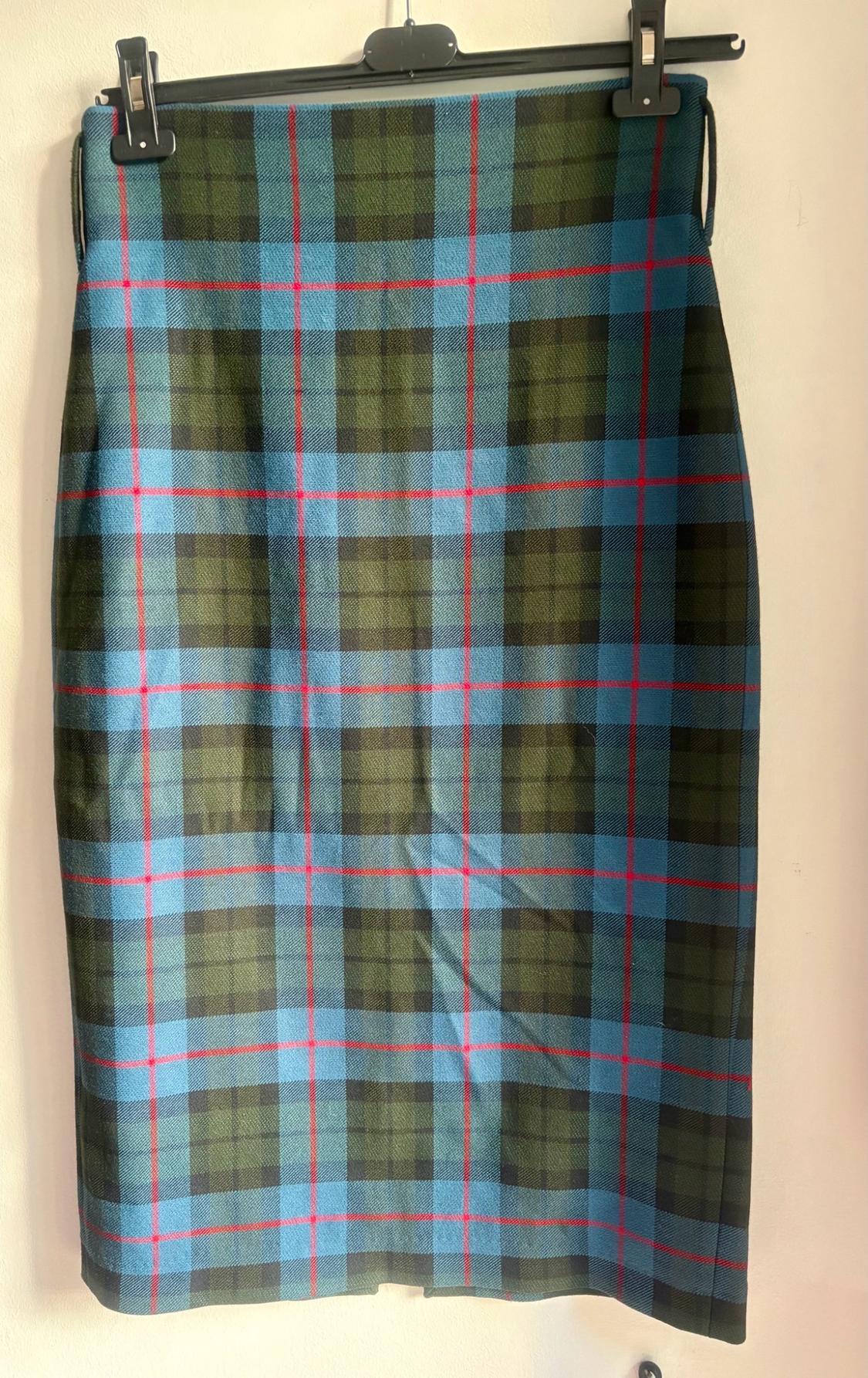 Straight plaid skirt in shades of blue, green and black with red lines, hanging from a black hanger against a white wall.