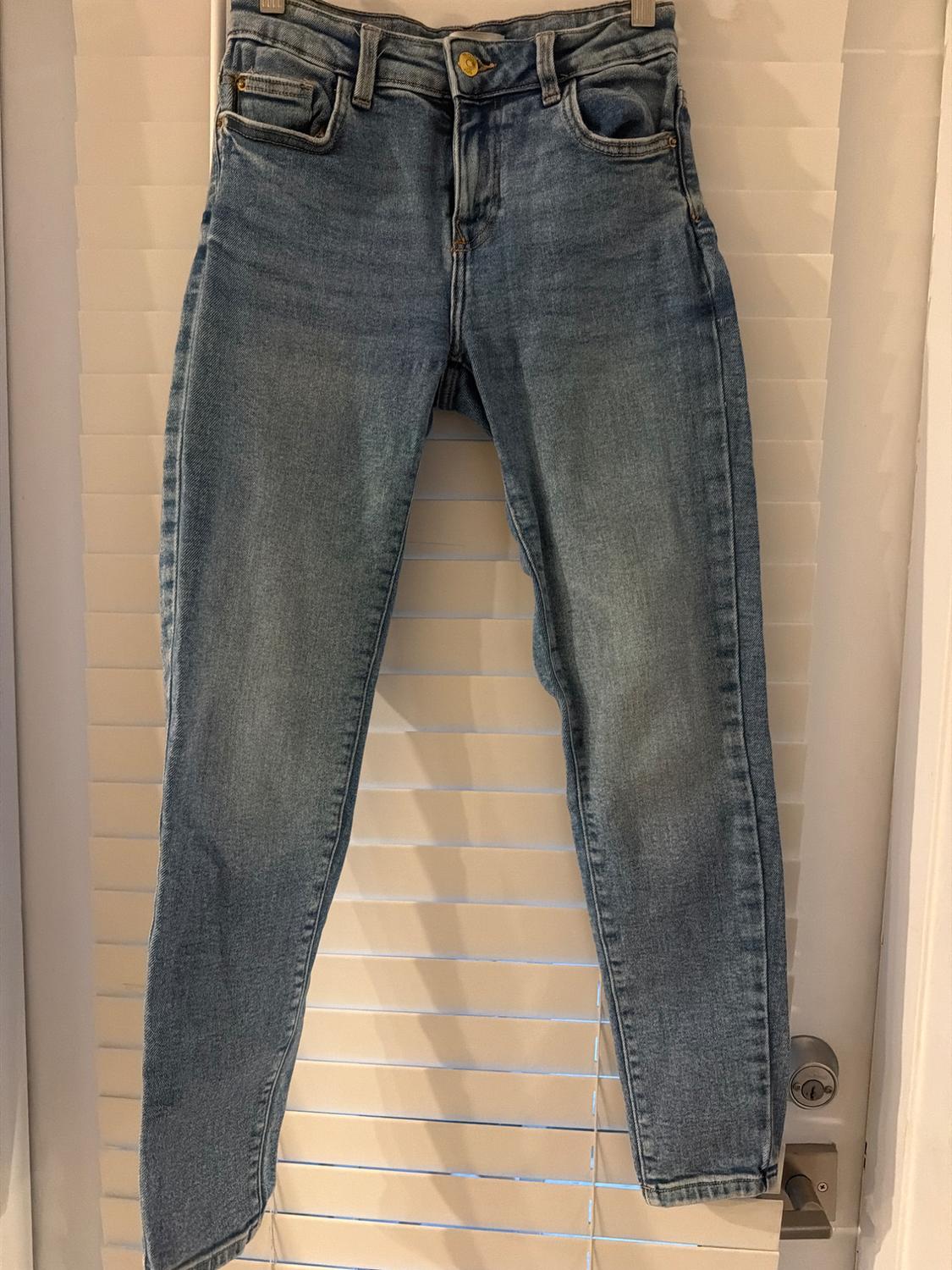 Slim-fit blue jeans hanging on a hanger in front of a white slatted door, conveying a casual style.
