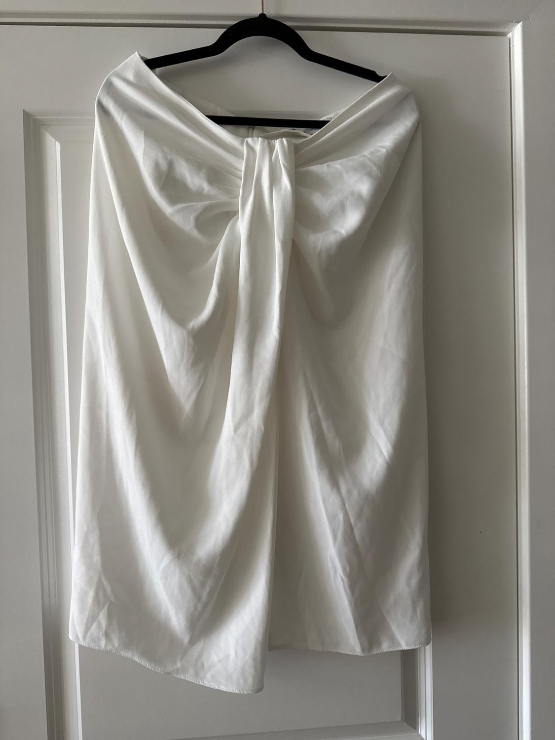 White draped skirt hanging on a black hanger over a white door. Soft fabric with elegant pleats.