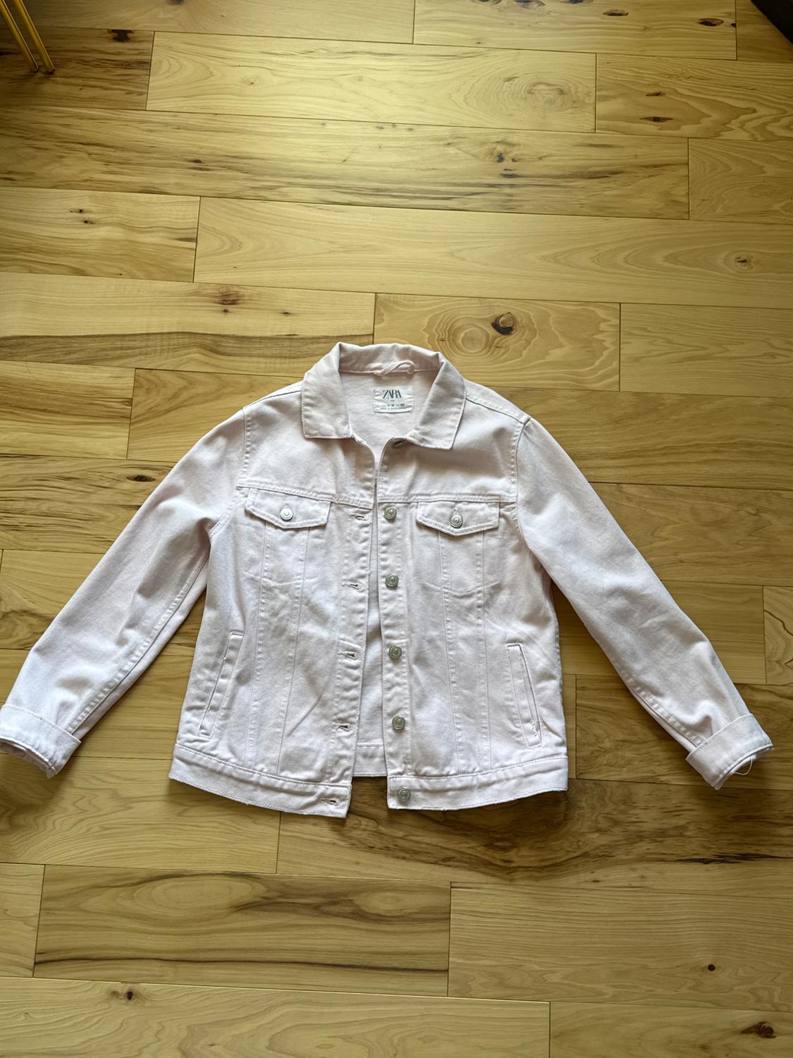 Light pink denim jacket with metal buttons, front pockets, and classic collar, on light wood floor.