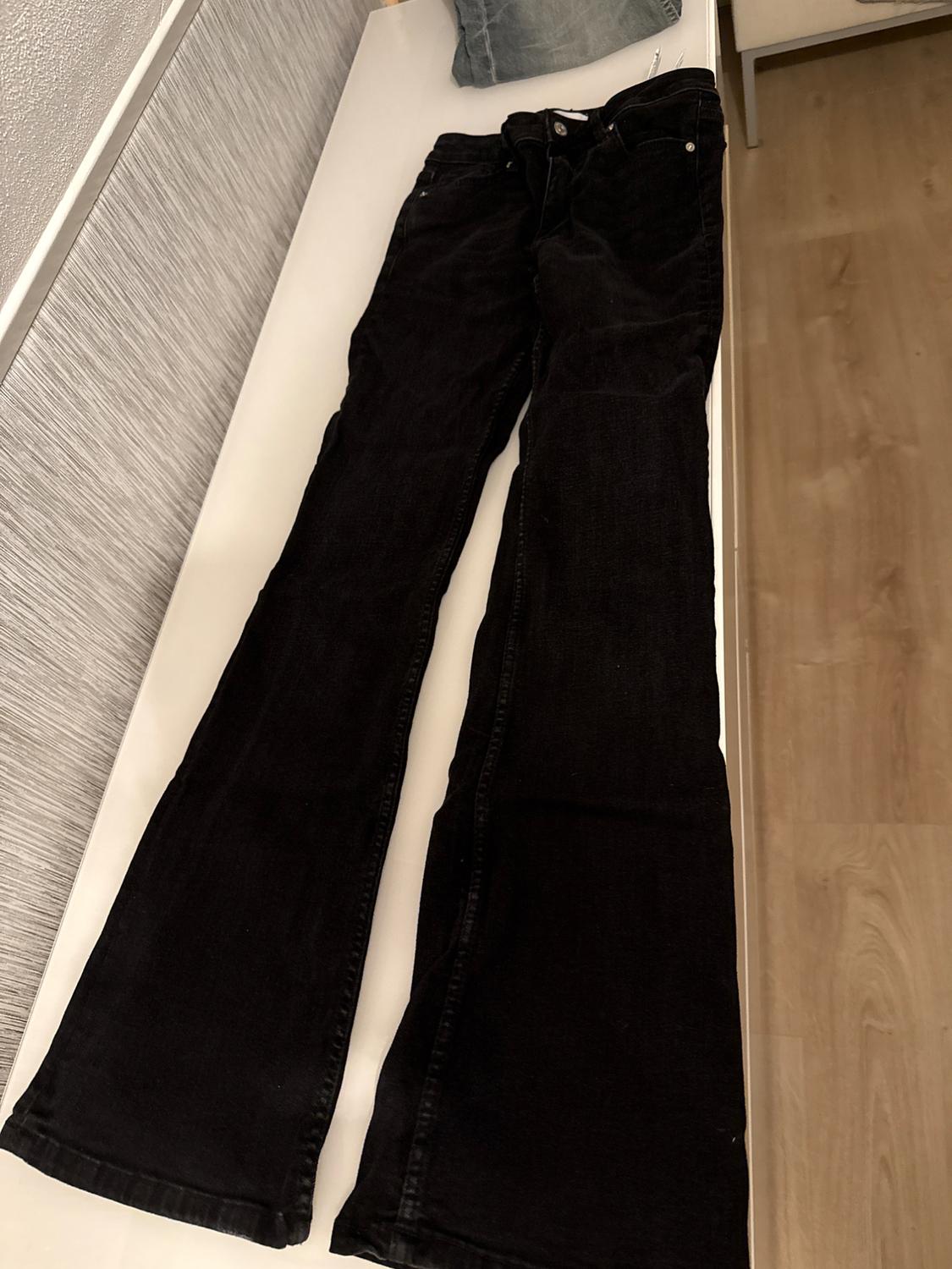 Black flared trousers placed on a white table, with a blue cushion in the background and wooden floor visible.