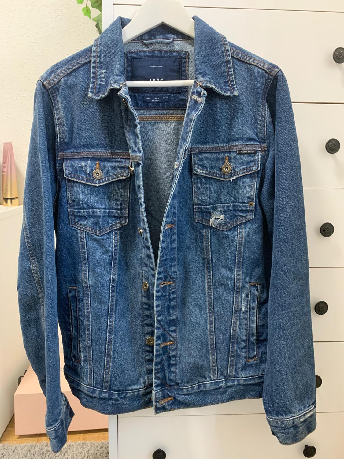 Front view of a blue denim jacket with front flap pockets and metal buttons.